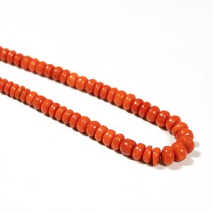 May include: A long necklace made of bright orange coral beads. The beads are round and have a smooth, polished finish.