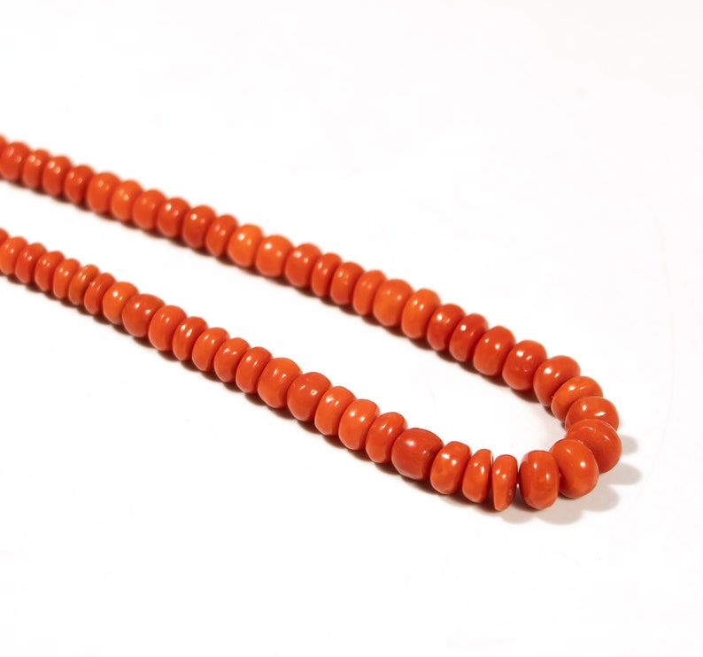 May include: A long necklace made of bright orange coral beads. The beads are round and have a smooth, polished finish.