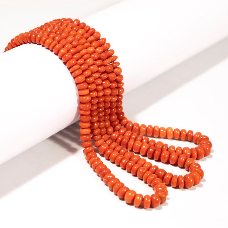 May include: A strand of bright orange coral beads, arranged in a loose coil on a white surface.