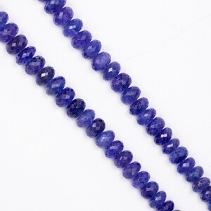 May include: Two strands of faceted, deep blue tanzanite gemstone beads. The beads are oval-shaped and strung together, creating a necklace or bracelet component. The background is plain white, highlighting the color and texture of the gemstones.