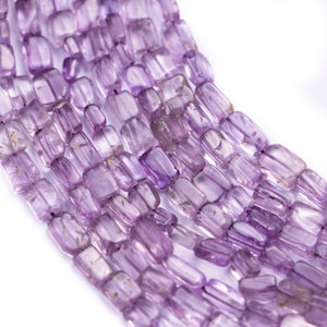 Puede incluir: Una hebra de cuentas de amatista de color púrpura claro, cada cuenta tiene forma de prisma rectangular.