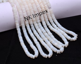 May include: A strand of white shell beads, approximately 16 inches long. The beads are round and flat, with a smooth, polished finish. The beads are strung on a clear thread. The strand is displayed on a white background. NK Impex is printed on the background.