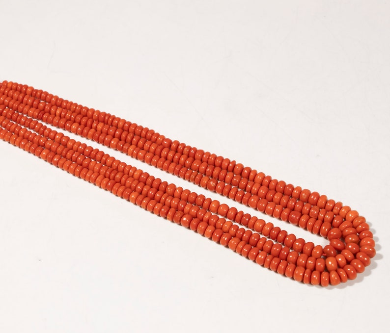 May include: A long strand of bright orange coral beads. The beads are round and uniform in size, creating a smooth and continuous line.
