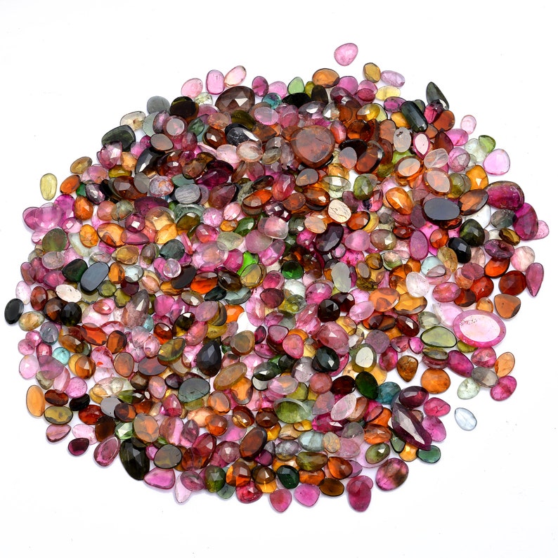 May include: A large collection of colorful, faceted gemstones in various shades of pink, green, brown, and black. The gemstones are oval-shaped and have a smooth, polished finish.