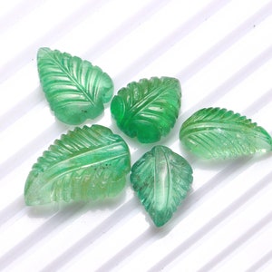 May include: Five green gemstone leaf-shaped beads. The beads are carved with detailed veins and are a light to medium shade of green.