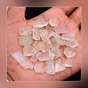 May include: A collection of clear, faceted, quartz crystals in various shapes and sizes. The crystals are arranged in a pile on a person's hand.