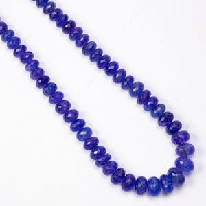 May include: A necklace of faceted, deep blue gemstones. The beads are strung together, creating a continuous strand of color. The gemstones have a polished, reflective surface, and the necklace is displayed against a white background.