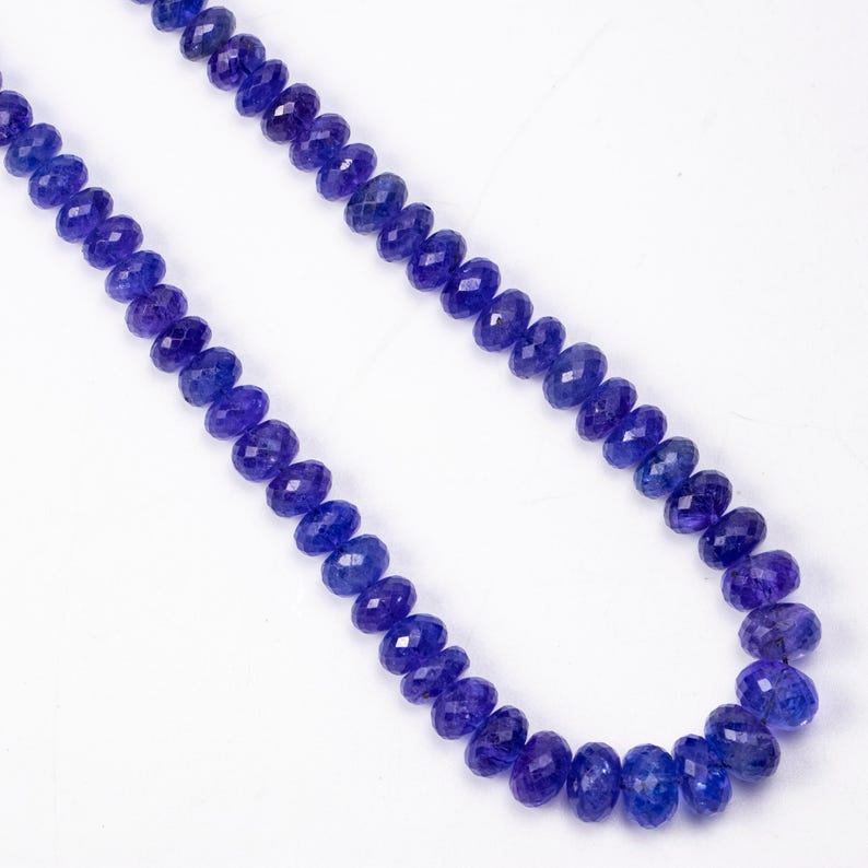 May include: A necklace of faceted, deep blue gemstones. The beads are strung together, creating a continuous strand of color. The gemstones have a polished, reflective surface, and the necklace is displayed against a white background.