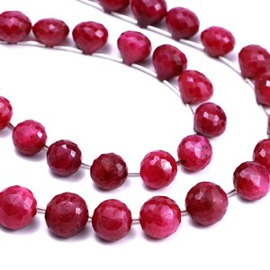 May include: A strand of deep red ruby beads, faceted and polished, strung on a silver wire. The beads are round and have a slightly irregular shape.