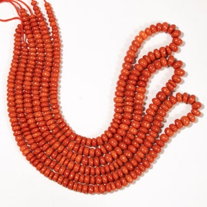May include: A strand of bright orange coral beads. The beads are round and smooth, and they are strung on a thin cord. The coral beads are arranged in a loose, flowing pattern.
