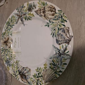 May include: White ceramic plate with a coastal design featuring seashells, starfish, and green foliage. The plate has a wide rim with the design around the edge. The text "Cherish the Ocean" is visible on a tag.