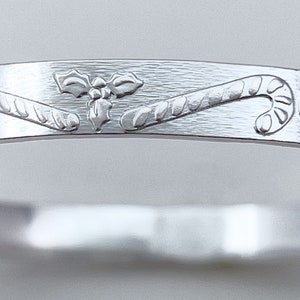 May include: Silver bangle bracelet with an engraved design of candy canes and holly leaves.
