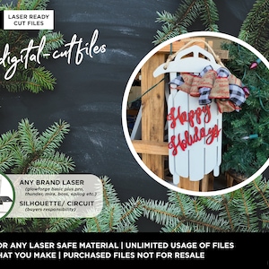 May include: A white wooden sled with the words "Happy Holidays" in red lettering. The sled is decorated with a red and white plaid bow and a burlap bow with the words "Merry Christmas" on it. The sled is hanging on a wooden fence with evergreen branches in the background.