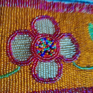 May include: Close-up of a beaded textile with a floral design. The flower is red with a center of multicolored beads. The background is orange with vertical beadwork, and the edges are trimmed in red.