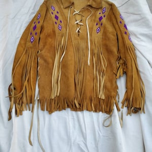 May include: A brown suede jacket with fringe and purple and white geometric embroidery. The jacket has a lace-up front and long sleeves.