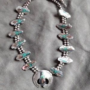 May include: A silver necklace with turquoise stones and a large pendant. The necklace is made of small silver beads and has a double strand design.