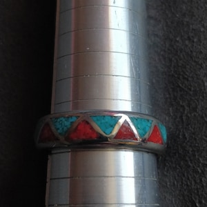 Peut inclure: Une bague en argent avec une bande de pierres turquoise et rouges disposées en forme de triangle.