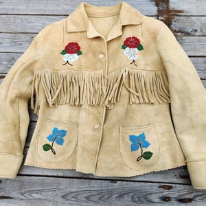 May include: A tan suede jacket with fringe detailing and beaded floral embroidery. The jacket has a button closure and two pockets.