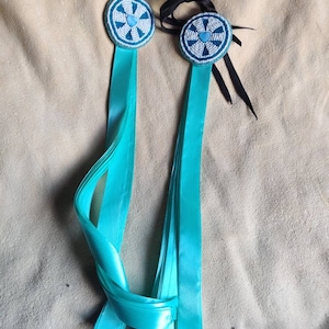 Peut inclure: Deux ornements circulaires en perles turquoise et blanches avec un motif de cœur au centre, chacun attaché à un long ruban turquoise.