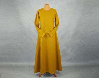 May include: Mustard yellow medieval-style dress with long sleeves and a flared skirt. The dress has a round neckline and is displayed on a mannequin. The dress is made of a thick, textured fabric. The bottom of the dress is flared.