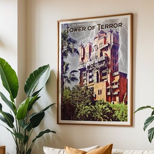 Op de afbeelding: Een ingelijste poster met een vintage ontwerp met een hoog, rood gebouw met de woorden "Hollywood Tower" en "Tower of Terror" in een vet, wit lettertype. De poster heeft een donkerblauwe achtergrond met een bliksemflits en groen gebladerte.