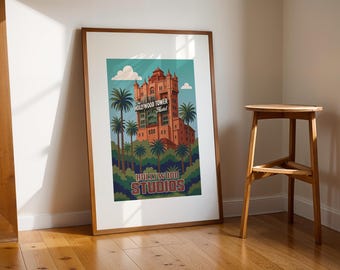 May include: Framed art print featuring a vintage-style illustration of the Hollywood Tower Hotel at Hollywood Studios. The artwork showcases the iconic building in shades of red and orange, surrounded by palm trees and the text "Hollywood Tower Hotel" and "Studios".