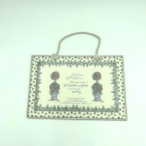 May include: Rectangular decorative plaque with a cream background, featuring floral and botanical illustrations. The plaque has a rope handle and includes the text "Each day is God's Gift to us. We must make it blossom and grow into a thing of beauty."