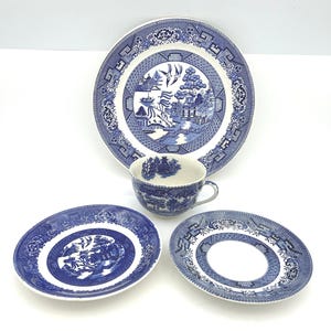 May include: A ceramic tea set featuring a blue and white willow pattern. The set includes one large plate, two smaller saucers, and one teacup. Each piece displays a detailed landscape illustration with birds, trees, and buildings in blue ink.