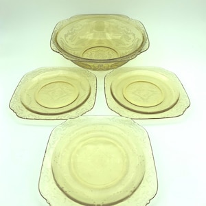 Puede incluir: Un juego de fuentes de vidrio color &aacute;mbar vintage. El juego incluye un cuenco grande y tres platos cuadrados. Cada pieza presenta un patr&oacute;n floral en relieve decorativo alrededor de los bordes y el centro. Los platos est&aacute;n colocados sobre una superficie blanca.
