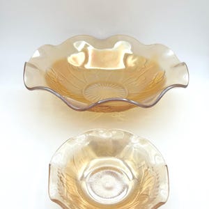 May include: Two iridescent amber-colored glass bowls. The larger bowl has a ruffled edge and a floral pattern. The smaller bowl is round with a ruffled edge and a floral pattern. Both bowls have a glossy finish.