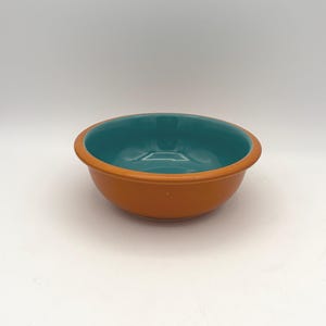 May include: A ceramic bowl with a teal interior and a brown exterior. The bowl has a rounded shape and a smooth, glossy finish. The bowl is empty and sits on a white surface. This bowl is suitable for serving food.