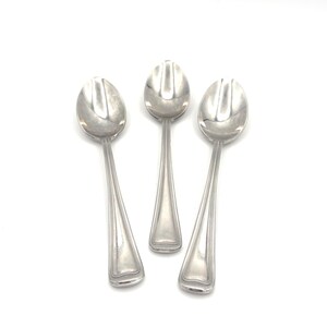 May include: Three silver-toned metal spoons arranged vertically. Each spoon features a polished oval bowl and a handle with a subtle, raised vertical line detail running along the edges, terminating in a rounded, slightly flared base.