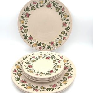 May include: A set of beige ceramic plates with a floral design. The plates feature a border of red, yellow, and green flowers and leaves. The set includes large dinner plates and smaller plates.