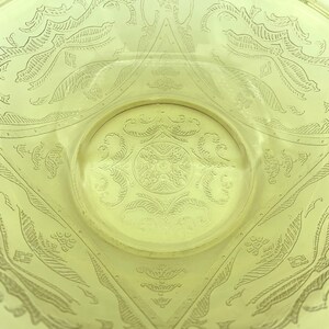 Puede incluir: Primer plano de un cuenco de vidrio amarillo con intrincados dise&ntilde;os grabados. El cuenco presenta un patr&oacute;n circular central rodeado de motivos geom&eacute;tricos y florales. El vidrio tiene una cualidad ligeramente transl&uacute;cida.
