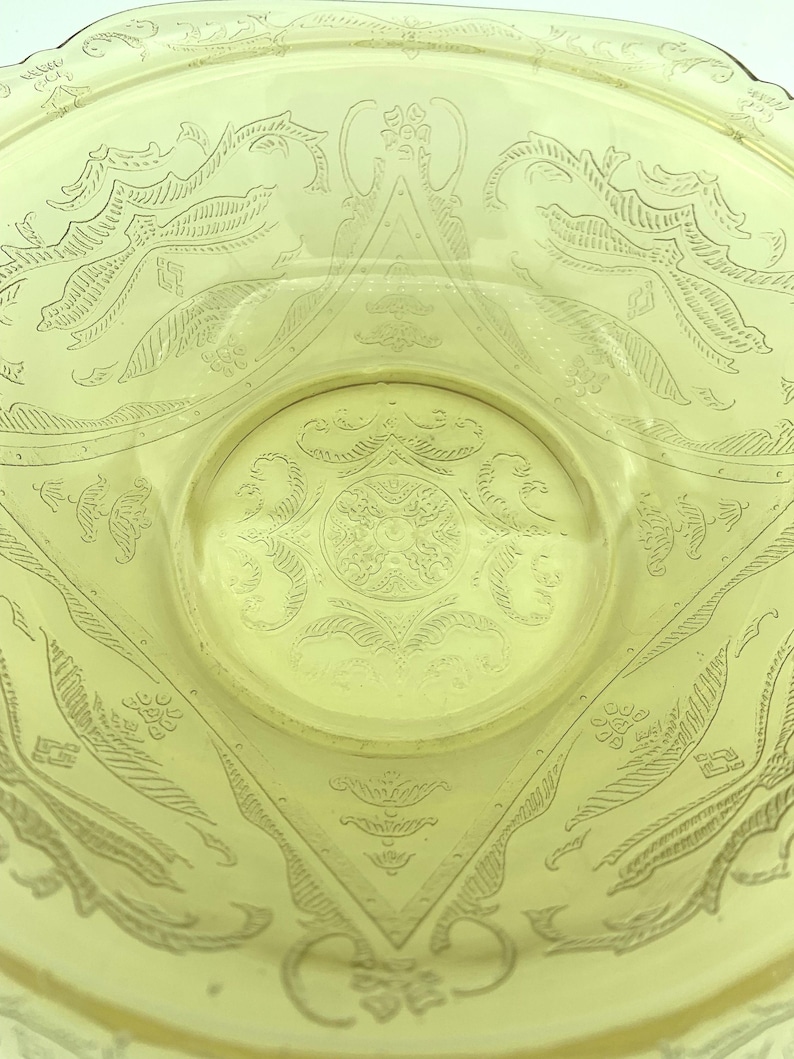 Puede incluir: Primer plano de un cuenco de vidrio amarillo con intrincados dise&ntilde;os grabados. El cuenco presenta un patr&oacute;n circular central rodeado de motivos geom&eacute;tricos y florales. El vidrio tiene una cualidad ligeramente transl&uacute;cida.