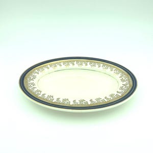May include: Oval serving platter with a cream-colored center and a navy blue border. The border is accented with a gold floral pattern. The plate is made of porcelain and is suitable for serving food.
