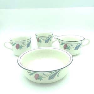 Puede incluir: Un juego de vajilla de cer&aacute;mica color crema que incluye dos tazas, una jarra para crema y un cuenco poco profundo. Cada pieza est&aacute; decorada con un borde azul oscuro y un patr&oacute;n floral de flores rojas y hojas azules sobre fondo blanco.