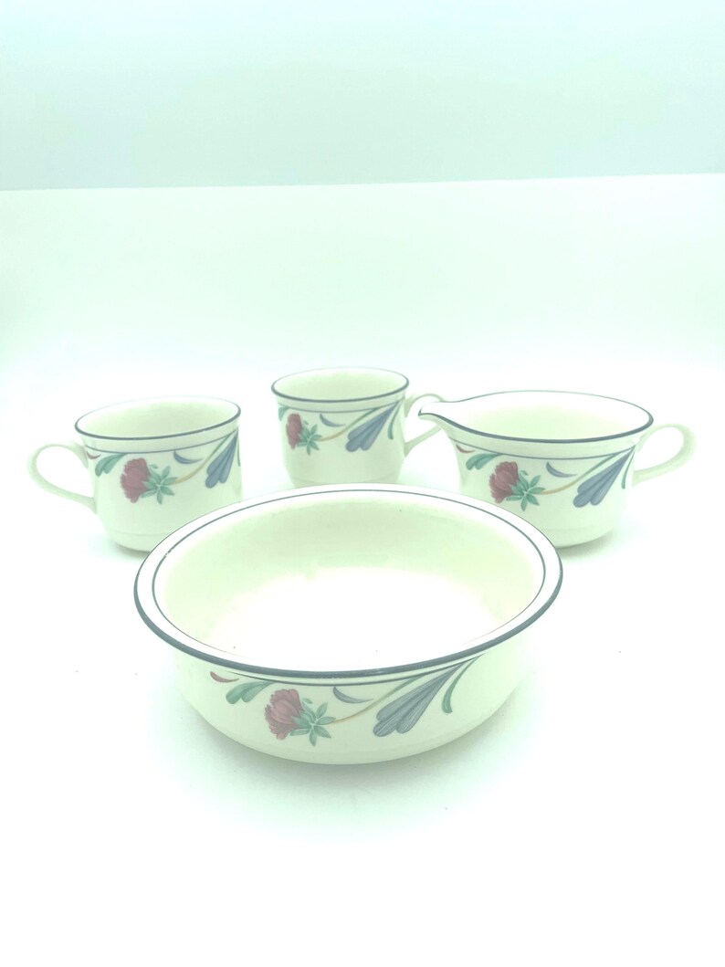 Puede incluir: Un juego de vajilla de cer&aacute;mica color crema que incluye dos tazas, una jarra para crema y un cuenco poco profundo. Cada pieza est&aacute; decorada con un borde azul oscuro y un patr&oacute;n floral de flores rojas y hojas azules sobre fondo blanco.