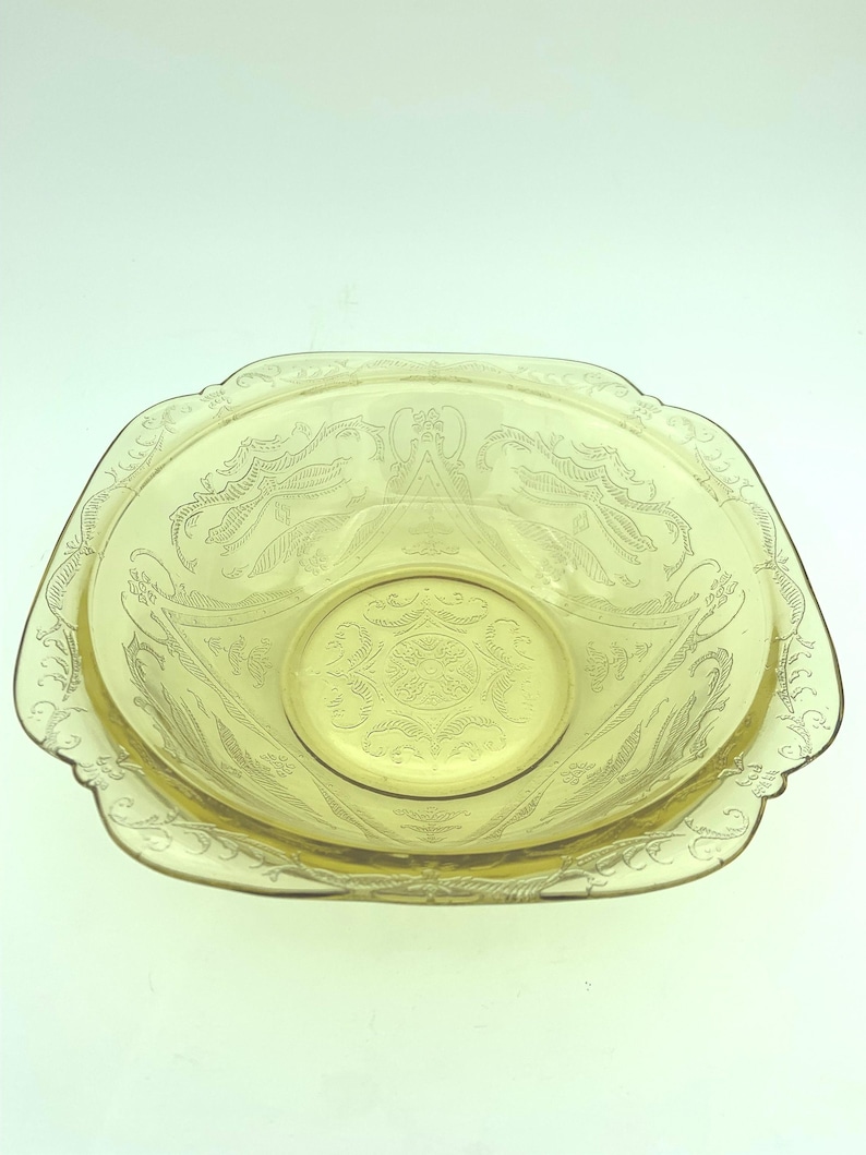 Puede incluir: Una fuente de vidrio te&ntilde;ido de amarillo con forma ovalada y un dise&ntilde;o decorativo grabado. La fuente tiene un borde festoneado y un cuenco central, m&aacute;s peque&ntilde;o y circular. El patr&oacute;n grabado incluye motivos florales y de volutas.