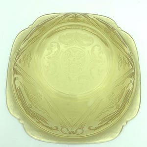 Puede incluir: Un cuenco de vidrio amarillo vintage con forma cuadrada y bordes festoneados. El cuenco presenta un dise&ntilde;o floral y geom&eacute;trico grabado. El cuenco es probablemente de la &eacute;poca de la Depresi&oacute;n y es una pieza decorativa.