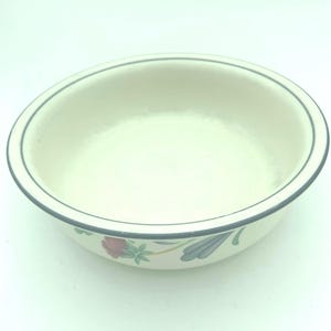 Puede incluir: Un cuenco redondo de cer&aacute;mica color blanco roto con un borde fino gris oscuro. El exterior del cuenco est&aacute; decorado con un patr&oacute;n floral que consiste en una flor rosa con hojas verdes y un dise&ntilde;o de hoja azul estilizada cerca de la base.