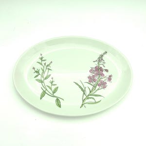May include: An oval-shaped pale mint green ceramic serving platter featuring a botanical illustration of two distinct flowering plants with green stems, leaves, and clusters of small pinkish-purple blossoms positioned on the surface of the dish.