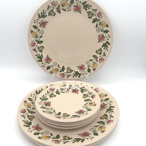 May include: A set of beige ceramic plates with a floral design. The plates feature a border of red, yellow, and green flowers and leaves. The set includes large dinner plates and smaller plates, perfect for a complete table setting.