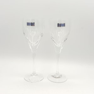 May include: Two clear crystal champagne flutes with a decorative etched design. Each glass has a long stem and a round base. The glasses have a label that reads "MARC" and "LE QUES".