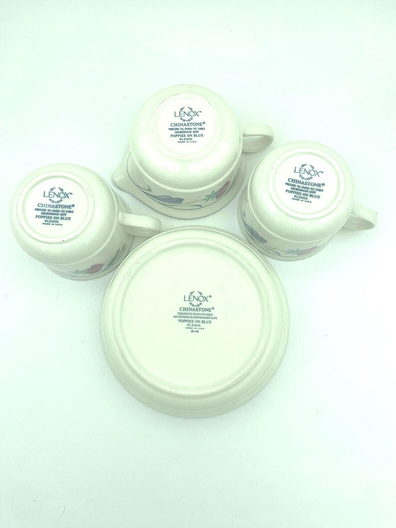 Puede incluir: Cuatro piezas de Chinastone color blanco roto de la colecci&oacute;n Lenox Poppies on Blue, incluyendo dos tazas, una jarra de leche y un platillo, mostradas boca abajo para exhibir el logo, el nombre del patr&oacute;n y el texto de apto para microondas.