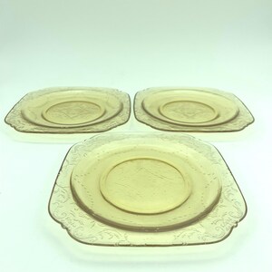 Puede incluir: Tres platos cuadrados de color &aacute;mbar con un patr&oacute;n floral decorativo en los bordes. Cada plato tiene un c&iacute;rculo central ligeramente elevado. Los platos son de vidrio y est&aacute;n dispuestos sobre una superficie blanca.