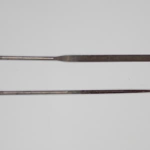 May include: Two metal files, one long and one short, on a white background.