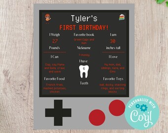 May include: A black and gray printable first birthday chart for a boy named Tyler. The chart includes information about his weight, height, favorite foods, toys, and books. The chart is decorated with a pixelated video game controller and a birthday cake.