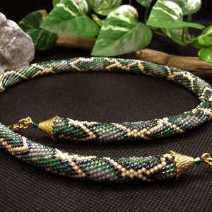May include: A green, white and grey beaded necklace with a gold clasp. The necklace is made of small, round beads that are arranged in a geometric pattern.