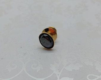 May include: A gold-toned tie tack with a black oval-shaped stone.